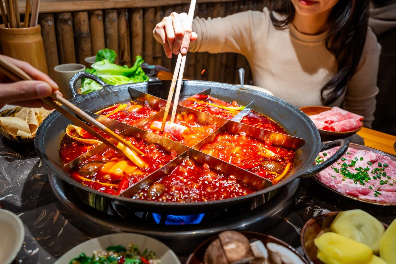 Couple sitting at a dinner table with a pot of Chongqing hotpot and dishes of raw meat and vegetables around the table
